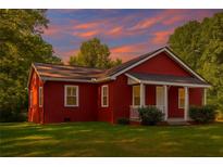 Charming red cottage with a cozy front porch and a well-maintained lawn surrounded by lush trees at 7880 Rivertown Rd, Atlanta, GA 30213