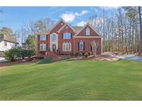 Charming two-story brick home featuring a well-manicured lawn, complemented by mature trees and beautiful landscaping at 455 Emerald Lake Path, Sugar Hill, GA 30518