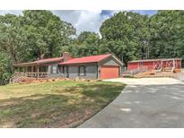 Charming gray home with red metal roof, attached garage, and grassy front yard surrounded by lush trees at 616 Rich Davis Rd, Hiram, GA 30141
