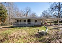 Single-story house with covered porch, carport, and landscaped yard on a sunny day, surrounded by trees at 3642 Highway 81, Oxford, GA 30054