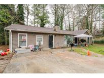 Tan single story home featuring a dark front door, brown roof and several deciduous trees surrounding it at 5461 Chuzzlewit Sw Ct, Lilburn, GA 30047