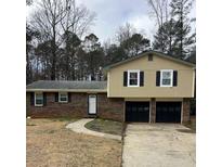 Split-level home with a brick facade, two-car garage, and mature trees in a residential neighborhood at 2193 Kings Forest Dr, Conyers, GA 30013