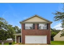 Two story brick home with a two car garage and manicured front lawn underneath a blue sky at 6595 Browns Mill Ferry Dr, Lithonia, GA 30038