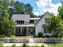 Charming two-story home with a white picket fence and lush landscaping, a metal roof, and modern windows at 9229 Selborne Ln, Chattahoochee Hills, GA 30268