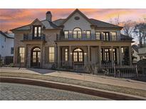 Elegant two-story home featuring a brick facade, wrought iron balconies, and a covered front porch at sunset at 440 Belada Blvd, Sandy Springs, GA 30342
