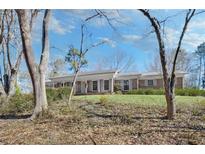 Rambling ranch-style brick home with a manicured lawn, trees, and a covered front porch at 6185 Heards Creek Dr, Atlanta, GA 30328
