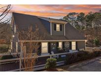 Charming home exterior with inviting front porch, gray siding, and beautiful landscaping at sunset at 5065 Sunrise Ln, Cumming, GA 30041