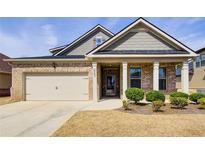 Charming brick home featuring a two-car garage, covered front porch, and manicured landscaping at 563 Carleton Pl, Locust Grove, GA 30248