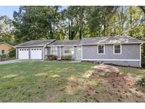 Charming home with a well-manicured lawn, gray siding, and a two-car garage nestled among mature trees at 4983 Needle Knob Ct, Lithonia, GA 30038