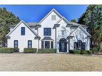 Elegant white home featuring a manicured lawn and sophisticated architectural design with black trim windows at 10683 Glenleigh Dr, Johns Creek, GA 30097