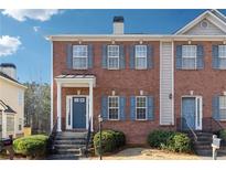 Charming brick townhome with a blue front door, well-maintained landscaping, and symmetrical window design at 5968 Eagle Tiff Ln, Sugar Hill, GA 30518