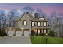 Stunning two-story brick home with a three-car garage and well-manicured lawn at dusk at 3610 Ansley Manor Ct, Cumming, GA 30028