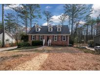 Charming brick home with dormer windows and landscaped front yard surrounded by mature trees on a sunny day at 1835 Tree Top Way, Marietta, GA 30062