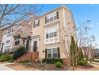 Charming two-story townhouse featuring light beige siding, dark shutters, a brick foundation and inviting front garden at 1262 Park Pass Row, Suwanee, GA 30024