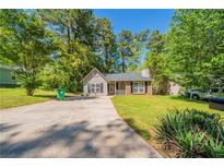 Charming single story home featuring mature landscaping, a spacious front yard and a paved driveway at 5500 Marbut Forest Way, Lithonia, GA 30058