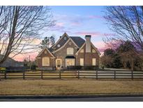 Beautiful brick and stone home with a well-manicured lawn and classic wooden fence at dusk at 6980 Polo Fields Pkwy, Cumming, GA 30040