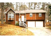 Charming home featuring a two-car garage, wood siding, and a manicured front lawn surrounded by mature trees at 5570 Deerfield Nw Pl, Kennesaw, GA 30144