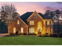 Stunning two-story brick home featuring manicured lawn, mature trees, and elegant architectural details at sunset at 2601 Floral Valley Dr, Dacula, GA 30019