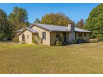 Charming brick home with a metal roof surrounded by lush greenery and a well-manicured lawn at 8736 Camp Rd, Winston, GA 30187