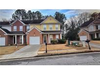 Two-story townhome featuring a brick and yellow exterior, attached garage, and manicured lawn at 553 Rockbridge Trl, Stone Mountain, GA 30083
