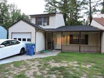 Two-story home with attached garage and front porch with railing in a lushly wooded suburban neighborhood at 402 Pine Tree Trl, Atlanta, GA 30349