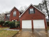 Two-story red brick home featuring a two-car garage and well-maintained landscaping at 105 Kentwood Springs Dr, Hampton, GA 30228