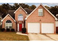 Charming two-story brick home with a well-manicured lawn, attached two car garage and a bright red front door at 11532 Ethan Ct, Hampton, GA 30228