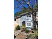 Two-story townhome with light blue siding and white trim surrounded by mature trees and overgrown front yard at 524 Northridge Crossing Dr, Atlanta, GA 30350