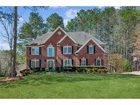 Beautiful two-story red brick home with a well-manicured green lawn and dark shutters on a sunny day at 7115 Doncaster Ct, Cumming, GA 30040