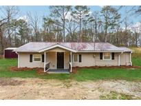 Charming single-story home with a metal roof, a small porch, neutral siding and mature trees in the background at 555 N Lake N Dr, Covington, GA 30016