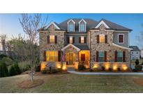 Charming stone-faced two-story home with manicured lawn and inviting entryway, illuminated by warm exterior lights at 4440 Croftshire Pl, Cumming, GA 30040