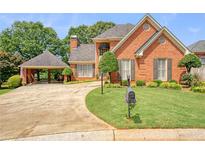 Charming red brick home featuring a two-car porte-cochere, manicured lawn and mature landscaping at 155 Oakpark Ct, Mcdonough, GA 30253