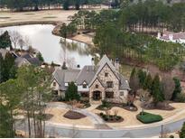 An aerial view of an elegant stone home on a well-manicured lawn, overlooking a serene lake at 938 Crescent River Pass, Suwanee, GA 30024