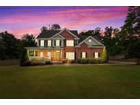 Stunning brick two-story home featuring a covered front porch, manicured lawn, and mature trees under a colorful evening sky at 100 Coldwater Creek Dr, Mcdonough, GA 30252