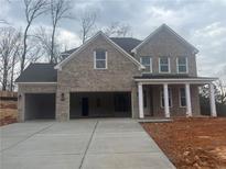 New construction two-story home featuring a two-car garage, a covered front porch, and a light gray brick facade at 6945 Melody Ridge Rd, Buford, GA 30518