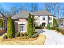 Elegant brick home featuring a well-manicured lawn, mature evergreens, and a spacious driveway on a sunny day at 4080 Glen Hill Ne Way, Marietta, GA 30066