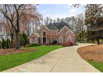 Beautiful brick home with manicured lawn, circular driveway, and mature trees at 5980 Mallet Ct, Cumming, GA 30040