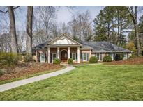 Charming brick home featuring a manicured lawn, mature trees, and a covered entrance at 11765 Mountain Laurel Dr, Roswell, GA 30075