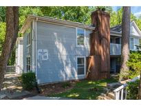 Exterior of a two-story condo with a brick chimney and light blue siding, set among lush trees in a green lawn at 6379 Wedgeview Ct # 6379, Tucker, GA 30084