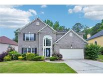 Charming two-story brick home featuring a well-manicured lawn, flowering shrubs, and an attached two-car garage at 2848 Stockbridge Way, Dacula, GA 30019