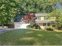 Charming yellow two-story home featuring a lush green lawn, mature trees, and an attached two-car garage at 320 Six Branches Ct, Roswell, GA 30076