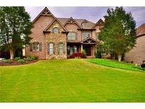 Beautiful two story brick home with stone accents, dormers, manicured landscaping, and a lush green lawn at 6040 Boulder Bluff Dr, Cumming, GA 30040