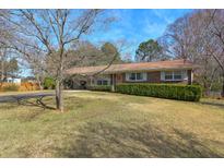 Charming brick home with a well-manicured lawn and mature trees under a blue sky at 3868 Sharon Dr, Powder Springs, GA 30127