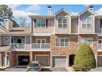 Attractive townhouse exterior with stone accents, covered parking, and balcony on a sunny day at 407 The Crossings Ln, Woodstock, GA 30189