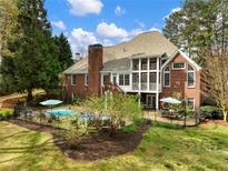 View of home's backyard with in-ground pool, brick exterior, large deck, and mature trees at 1544 Blue Bird Way, Cumming, GA 30041