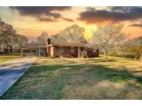 Charming brick home with a covered carport and a spacious front yard, set against a vibrant sunset sky at 1715 Highway 11 N, Social Circle, GA 30025