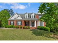Traditional brick home featuring a welcoming front porch with white columns and a beautifully manicured lawn at 711 Wilhaven Ct, Loganville, GA 30052