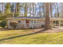 Charming single-story home with a carport and well-manicured lawn and an inviting red front door at 3475 Glensford Dr, Decatur, GA 30032