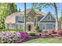 Charming home with a stone facade, gray siding, and beautiful landscaping including pink and purple flowers in the front yard at 4800 Island Ne Vw, Roswell, GA 30075