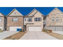 Charming townhome showcases a two-car garage and neutral brick exterior against a vibrant blue sky at 2463 Quay Rdg, Lawrenceville, GA 30044